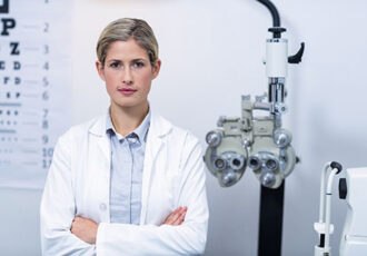 Portrait of beautiful female optometrist standing with arms crossed in ophthalmology clinic