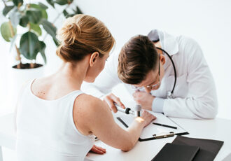 selective focus of woman looking at dermatologist examining skin in clinic